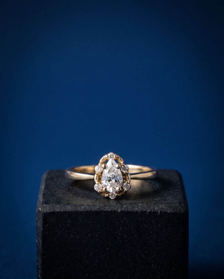 Gold ring with a pear-shaped lab-grown diamond surrounded by a halo of round stones